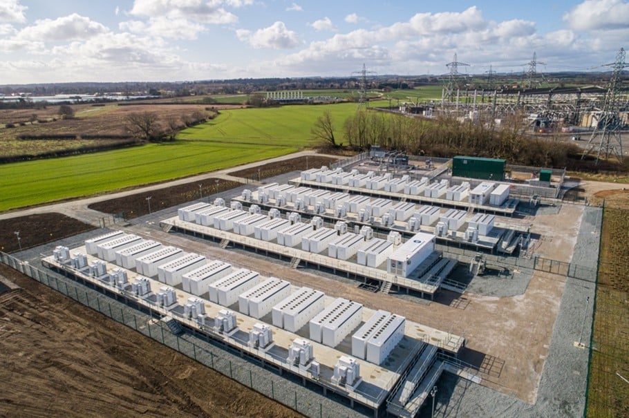 A battery storage site next to a green field on the left. Cloudy skies and concrete ground