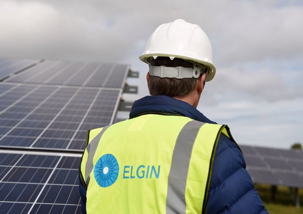 a man in an elgin branded hi vis vest stands by a solar panel