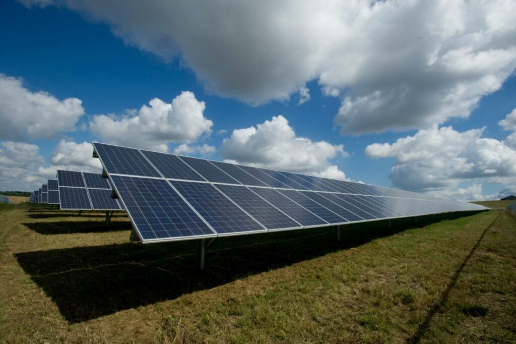 solar panels under a blue sky with large puffy clouds.