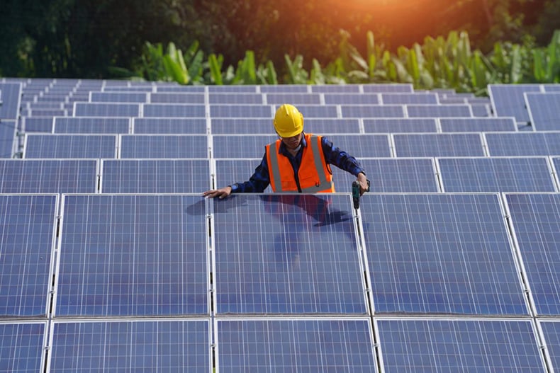 a man in high visibility safety gear stands surround by rows of solar panels
