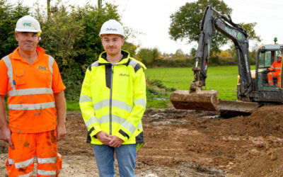 Two white men in hi-vis safety gear stand at a construction site