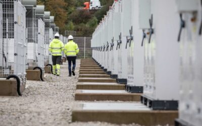 Two men in hi-vis jackets walk next to BESS units