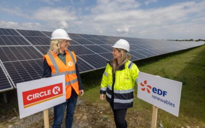 Female Circle K and EDF renewables represnetatives stand next to branded signs in front of solar PV panels.