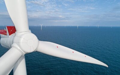 A wind turbine close up with blue sea and sky behind