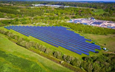 An aerial shot of a solar farm surrounded by green trees.