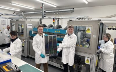 researchers in lab coats hold up a thin film solar cell in a lab