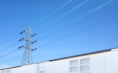 White BESS units underneath a blue sky with a pylon and electricity wires above