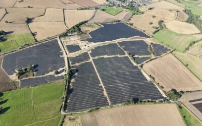An overhead photograph of a large solar farm situated among green fields