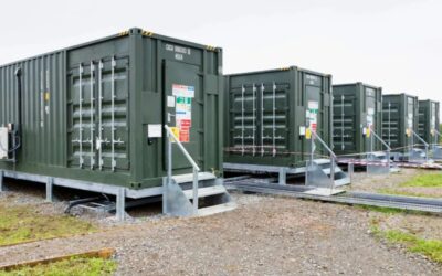 Three dark green battery energy storage units under a cloudy sky