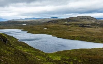 a wide sweeping view of Scotland's Loch Ness with blue skies, rugged green landscapes and a large body of water