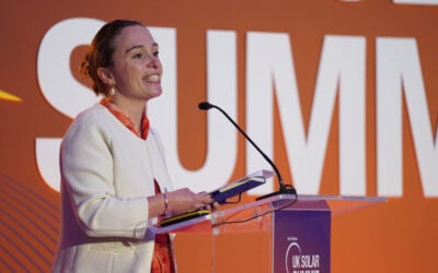 a woman speaks at a podium with a uk solar summit banner behind her