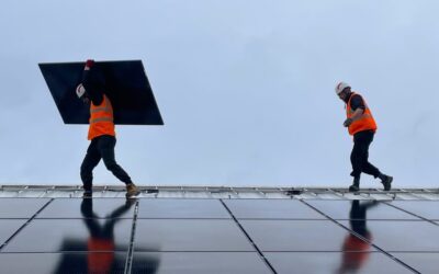 two men carry solar panels along a roof