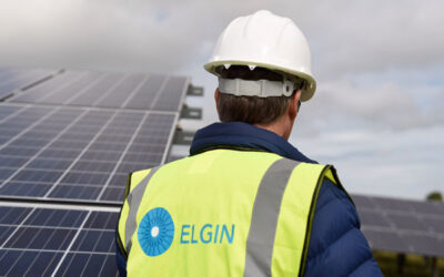 a man in an elgin branded hi vis vest stands by a solar panel