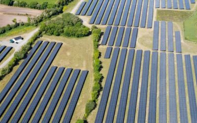 a field of solar panels from above with a small cottage in the background